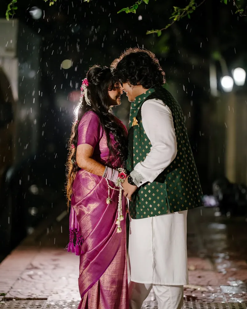 Aazrin in a purple silk saree and Jabir in a green bandi over a white panjabi, forehead to forehead in the rain on the Holud night