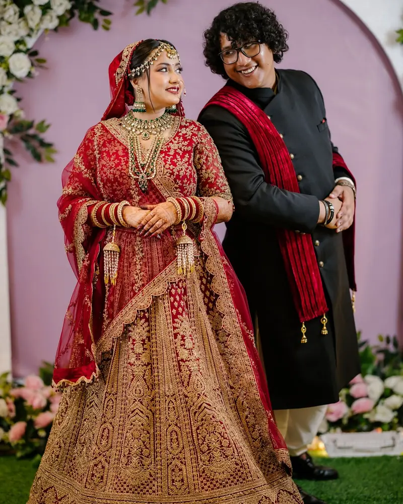 Aazrin in a red lehenga and Jabir in a black sherwani with a red scarf, smiling at each other at the wedding