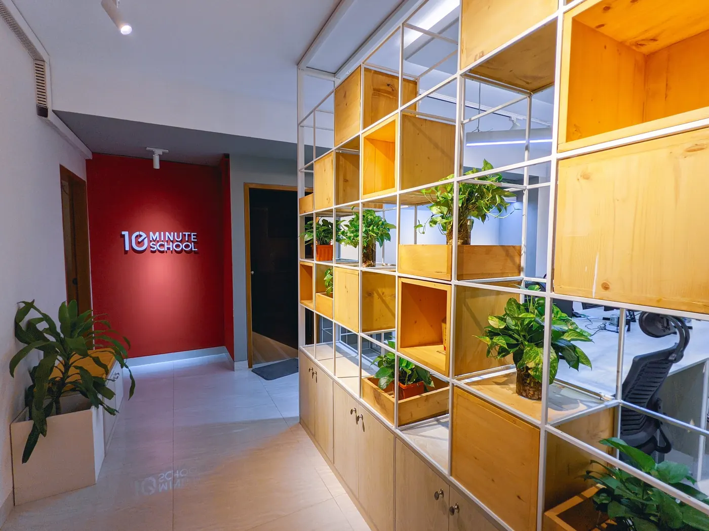A red wall with the logo, beside shelves of plants