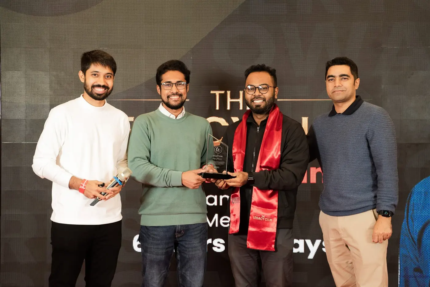 Asif Hossain (third from left) receives his 6-year Legacy Club crest on stage, in the red scarf