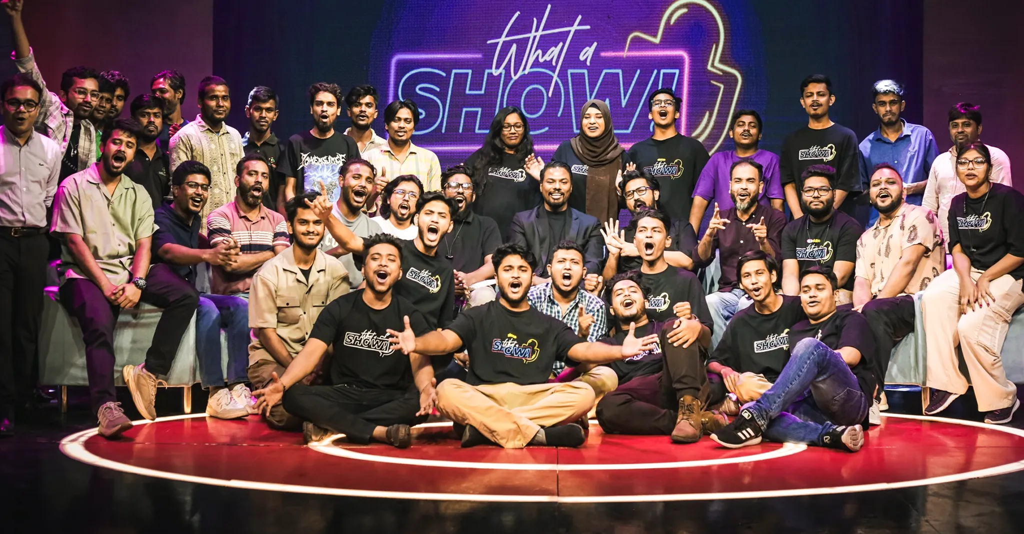 The What a Show! team gathered on stage under the neon sign